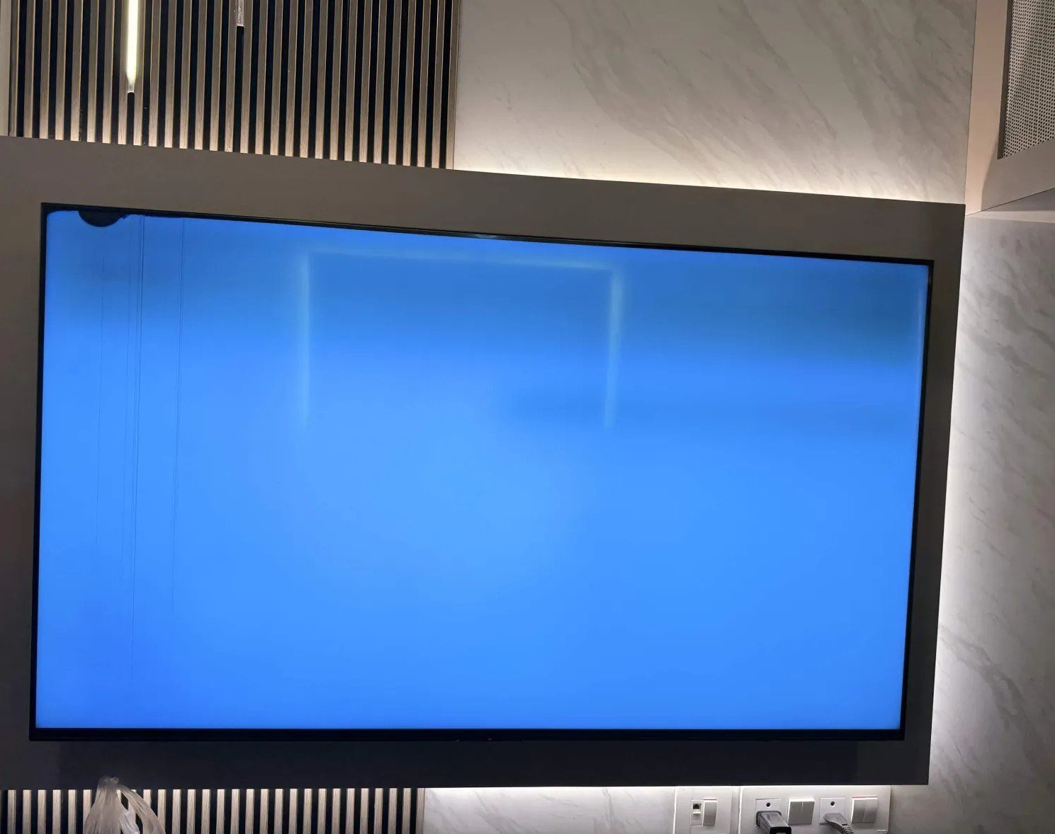 The full TV on its wall mount during the blue RGB test: dark patch and lines top-left, frame and all four corners spotless